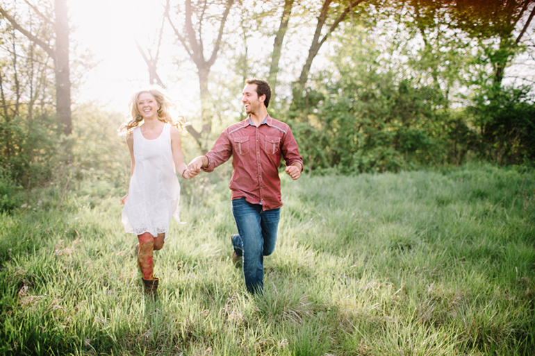 couple holding hands running through a field