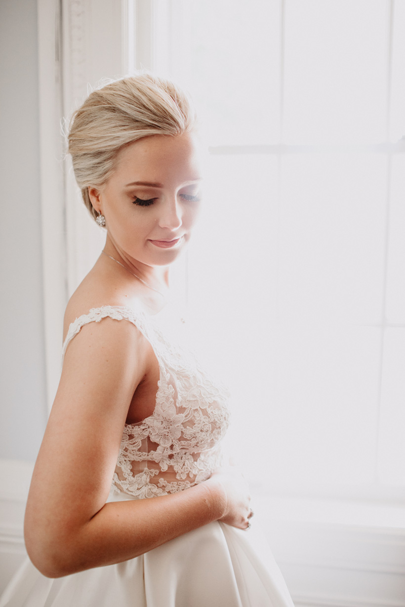 bride backlit in winow in lace wedding dress